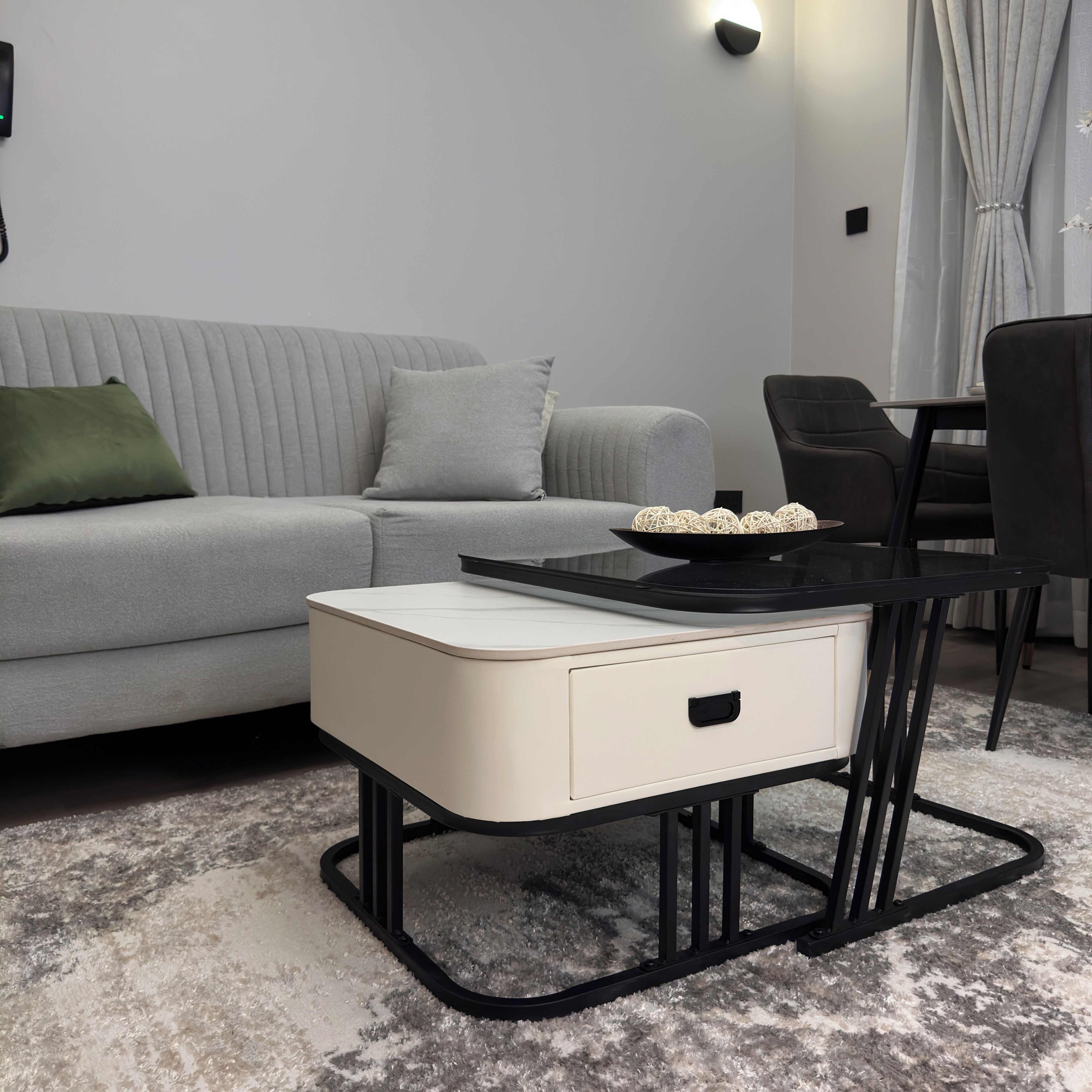 Una sala de estar moderna con un sofá gris, una mesita auxiliar blanca, una mesa de centro negra y una silla negra.