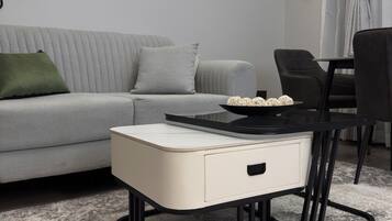 Una sala de estar moderna con un sofá gris, una mesita auxiliar blanca, una mesa de centro negra y una silla negra.