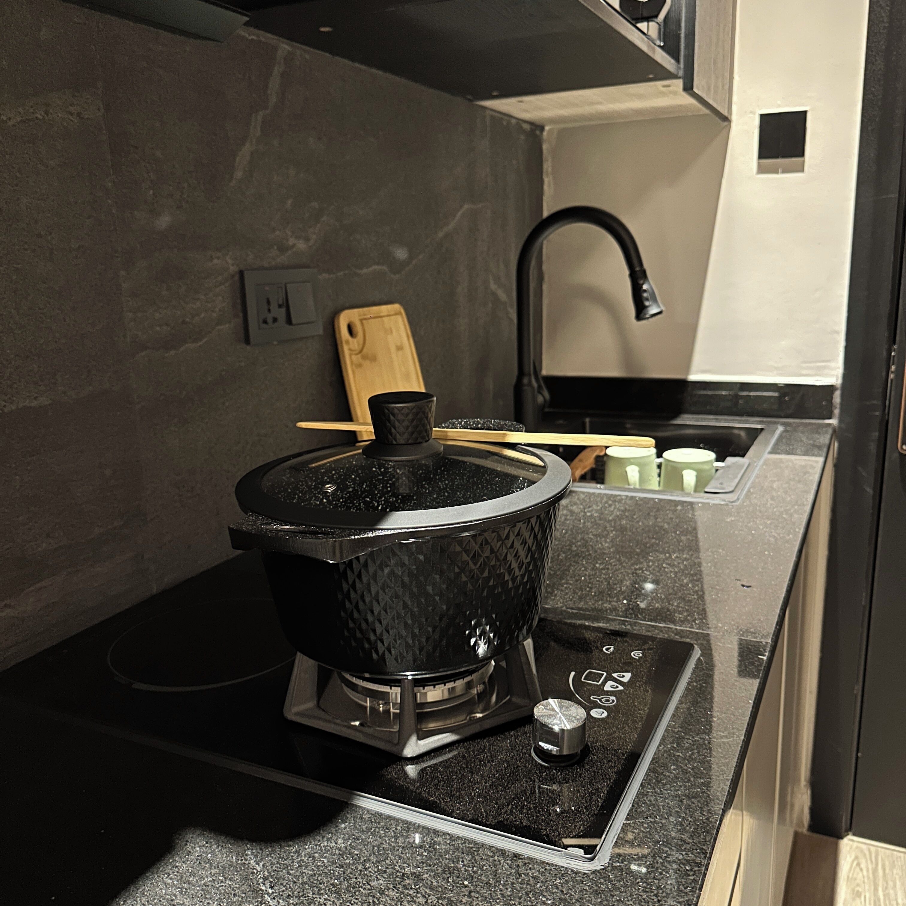 A kitchen with a black electric stove, a wooden cutting board, and a black faucet.