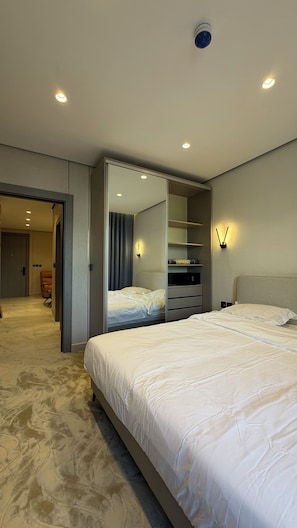 Une chambre d’hôtel moderne, dotée d’un grand lit, d’un dressing et d’une salle de bain visible à travers une porte ouverte.