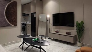 Een moderne woonkamer met een flatscreen televisie, een salontafel, een bank, een potplant en inbouwspots.