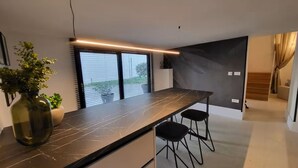 Een moderne keuken met een marmeren aanrecht, twee zwarte barkrukken, een vaas met groene planten en een uitzicht door grote ramen.