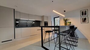 Een moderne keuken met een centraal kookeiland, barkrukken en een hanglamp.