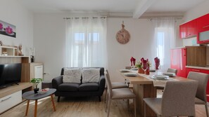 Ein modernes Wohnzimmer mit Sofa, Fernseher, Esstisch für zwei Personen und einer roten Küchenzeile.
