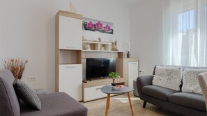 Ein modernes Wohnzimmer mit Flachbildfernseher, einer Couch, einem Couchtisch und einer Zimmerpflanze.
