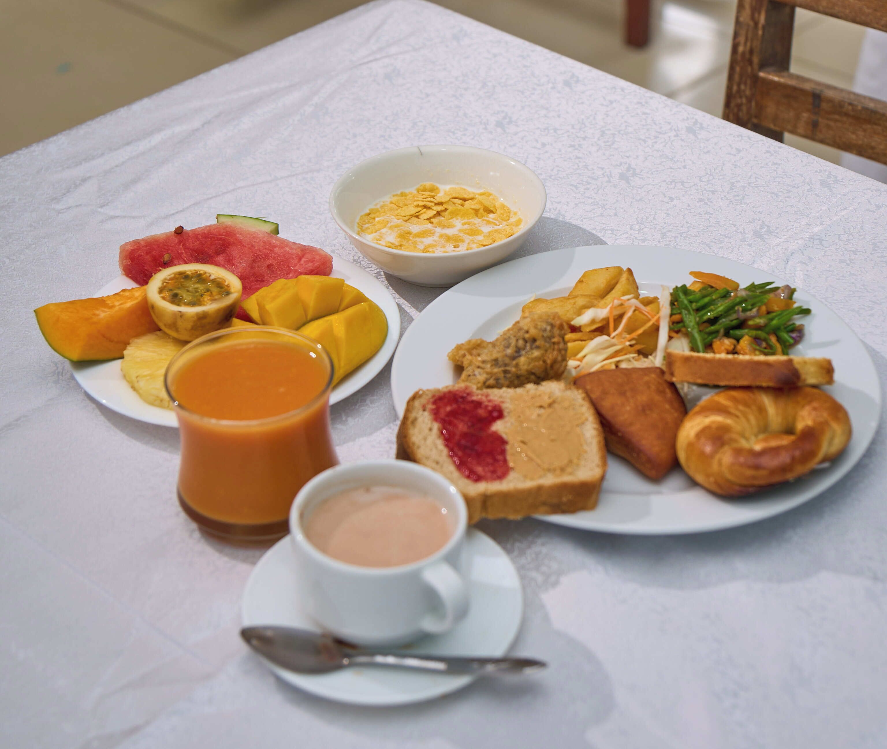 Ett frukostbord med tallrikar fyllda med mat, en skål med flingor, ett glas apelsinjuice och en kopp kaffe.