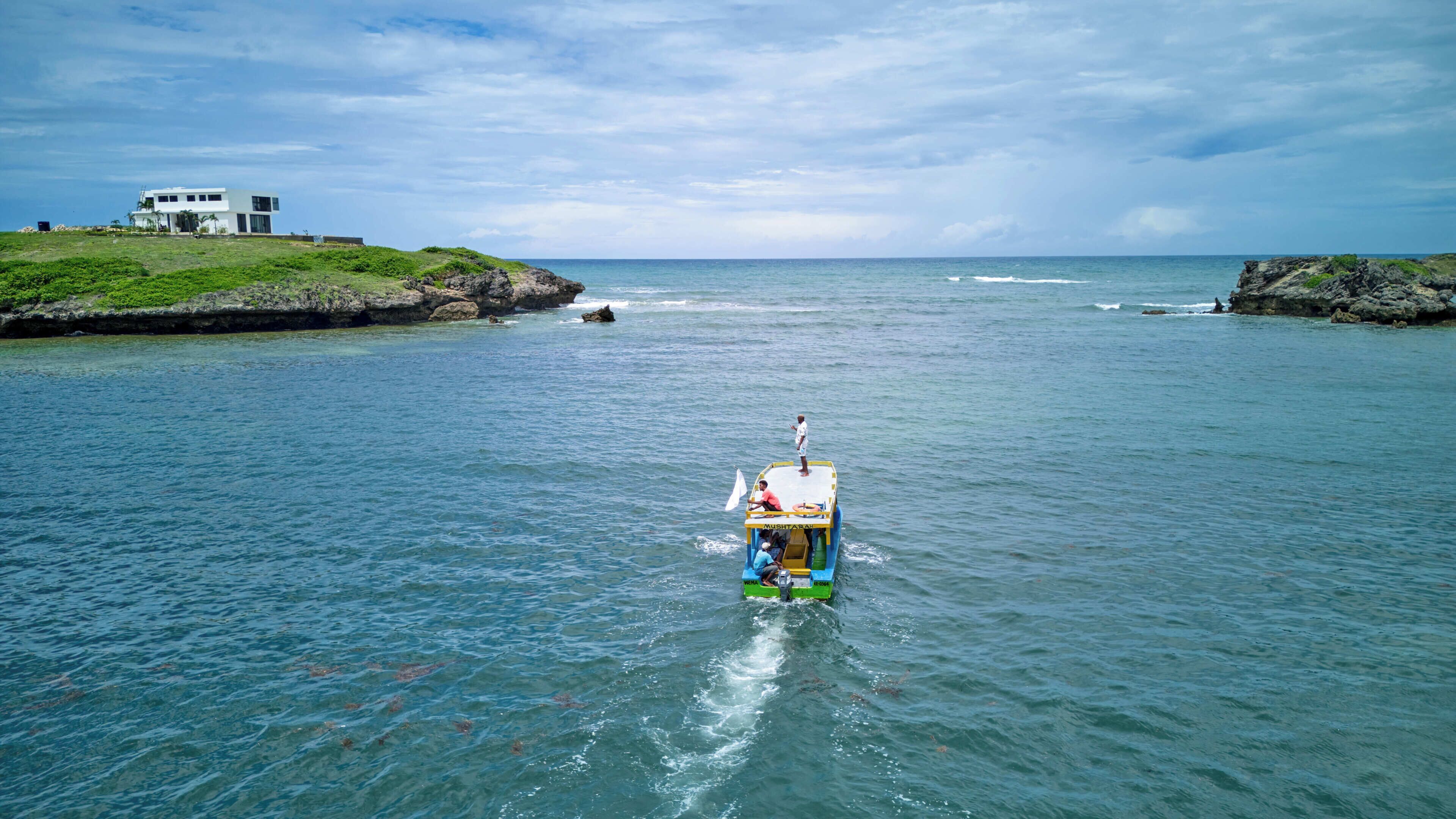 A boat with passengers, a rocky shoreline, and a building in the background.