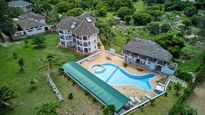 Una casa grande con piscina, un porche cubierto y una construcción con techo de paja.