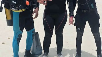 Three individuals in scuba diving gear standing on a sandy surface.