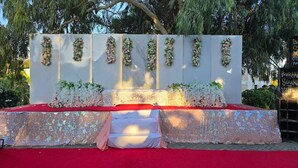 Un escenario con alfombra roja, decoración floral y un telón de fondo blanco.