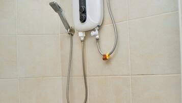 Een badkamer met een in de muur gemonteerde douche, een handdouche en een wastafel in de hoek met een kraan.