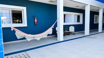 A blue exterior wall with a white tiled floor, a red fire extinguisher, a white hammock, and two wooden chairs.