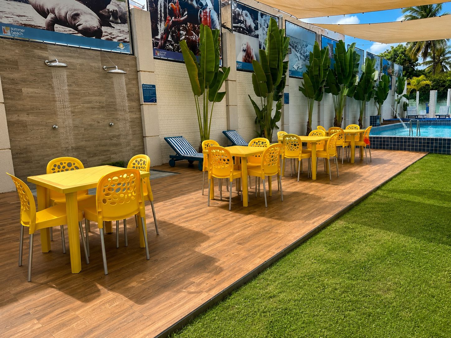 A poolside area with yellow tables and chairs, a wooden deck, and a grassy area.