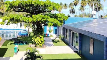 Un hotel con piscina, un espacio exterior cubierto y vistas a palmeras.
