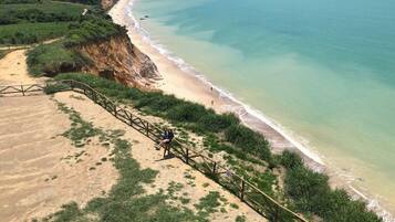 Eine Küstenlandschaft mit einem Sandstrand, einer Holztreppe, die zum Ufer führt, und freiem Blick auf den Ozean.