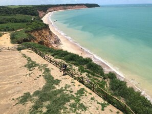 Paisaje costero con playa arenosa, una escalera de madera que baja hacia la orilla y una vista despejada del océano.