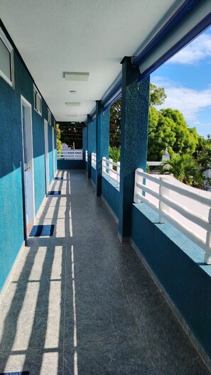 Un pasillo cubierto con suelo de baldosas, barandillas blancas y vistas a zonas verdes.