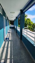 Uma galeria coberta com piso de azulejos, corrimãos brancos e vista para o verde.