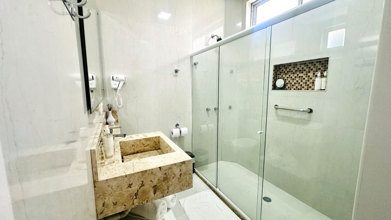 A modern bathroom with a marble sink, glass shower enclosure, and a towel rack.
