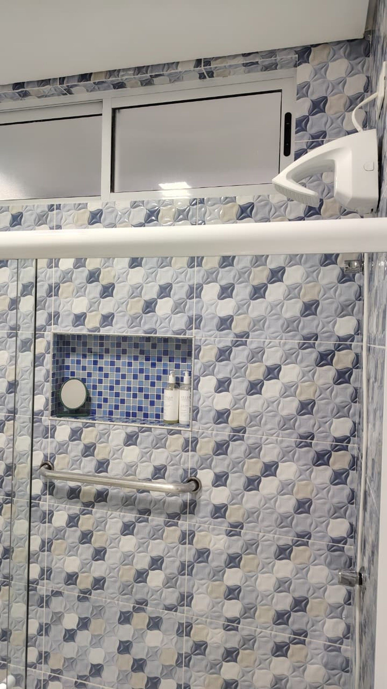 Casa de banho com parede de azulejos estampados, cabine de duche em vidro e toalheiro branco.