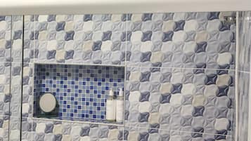 Casa de banho com parede de azulejos estampados, cabine de duche em vidro e toalheiro branco.