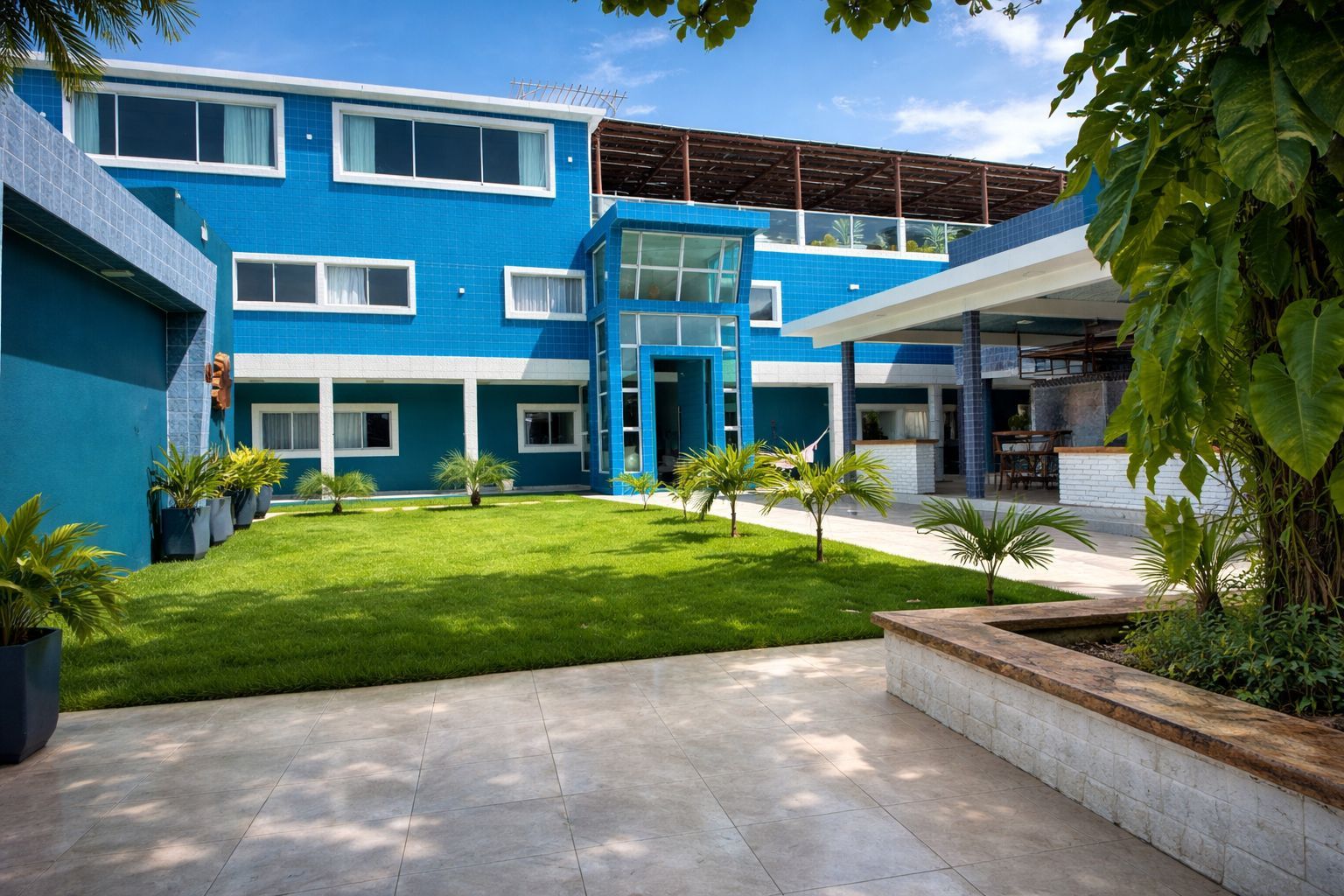 A modern building with a blue exterior, a well-maintained lawn, and potted plants.