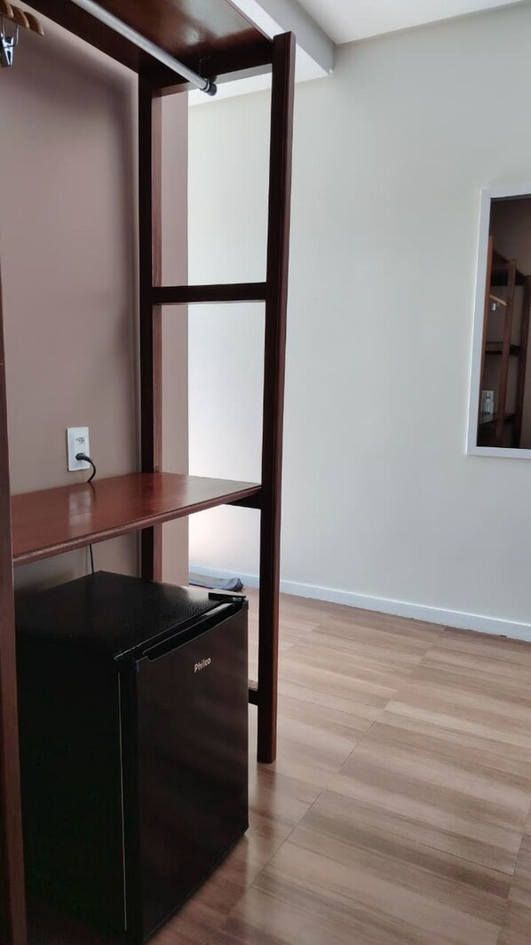 Una habitación con piso de madera, un refrigerador negro y una pared blanca con ventana.