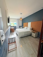 Quarto moderno com cama, mesa de cabeceira e um pequeno espaço de estar.