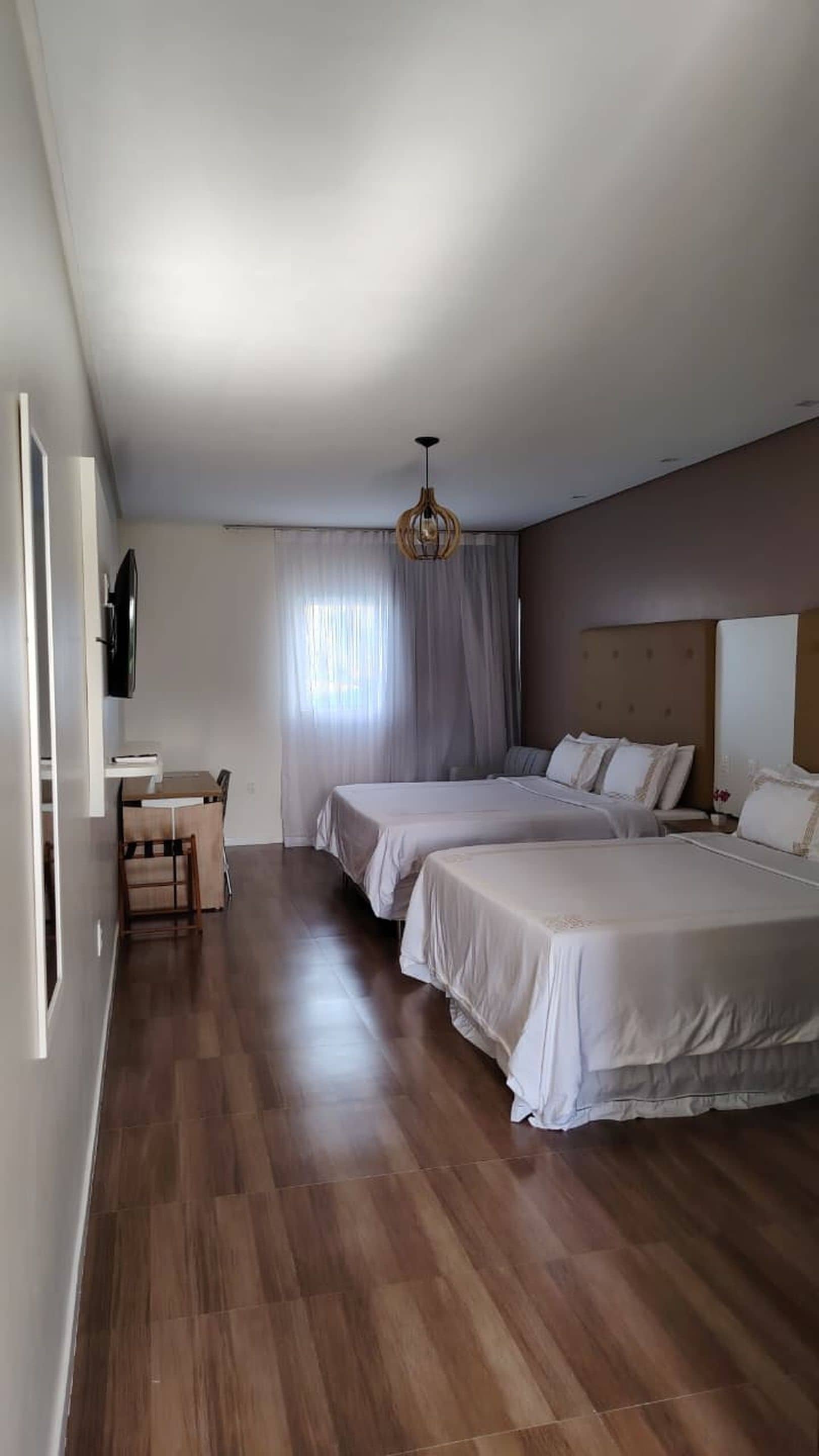 Habitación de hotel con piso de madera, dos camas, un escritorio y una televisión.