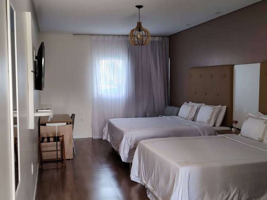 A hotel room with a wooden floor, two beds, a desk, and a TV.
