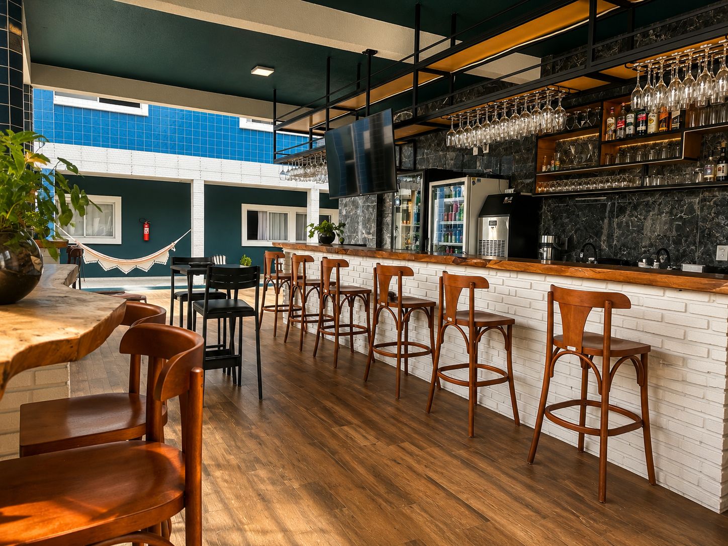 Un área de bar con sillas de madera, una barra con televisor y vistas a un edificio azul.