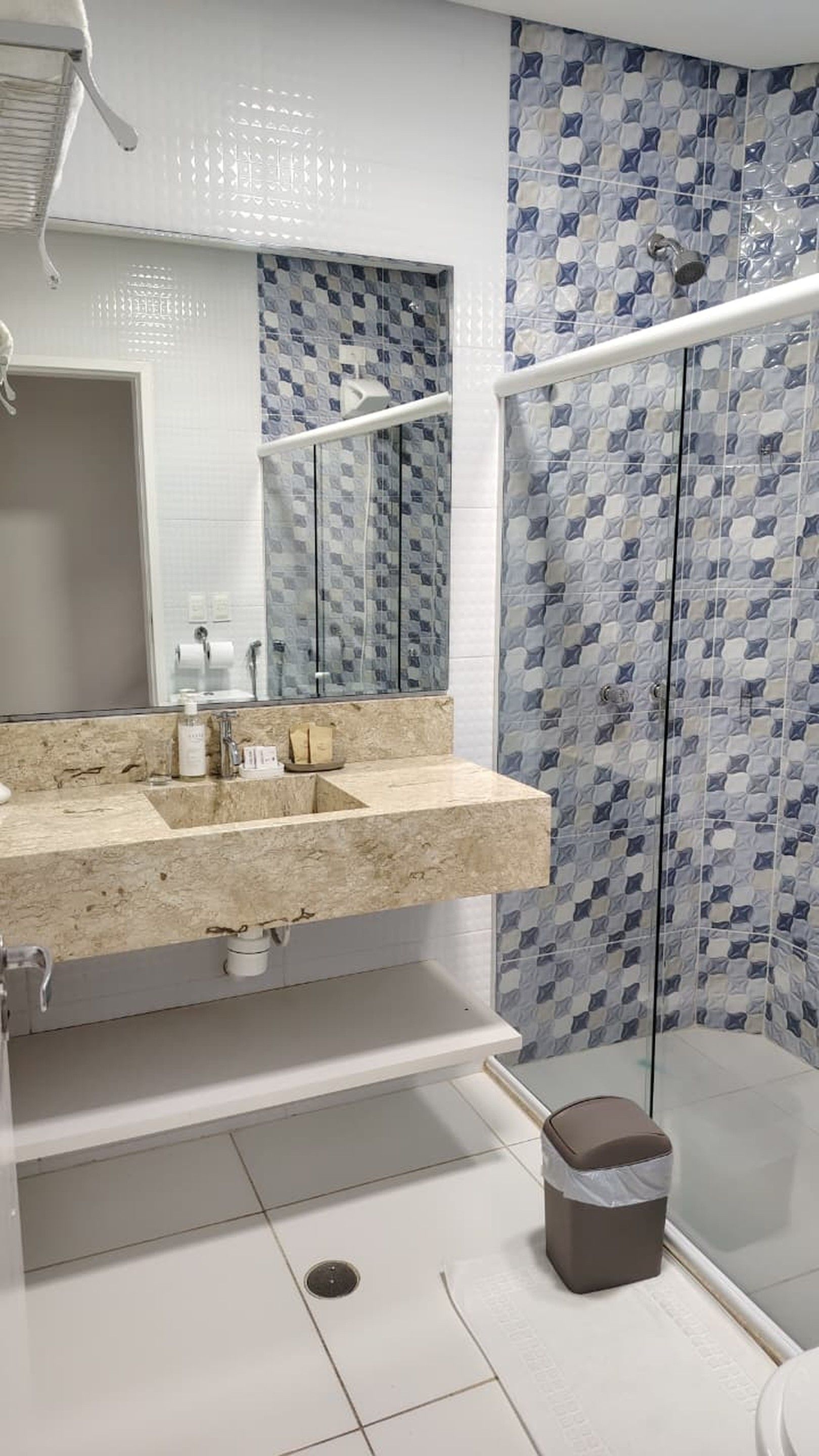 Un baño con lavamanos de mármol, cabina de ducha con paredes de vidrio y pared con azulejos.
