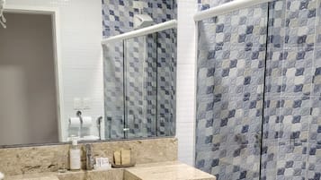 Un baño con lavamanos de mármol, cabina de ducha con paredes de vidrio y pared con azulejos.