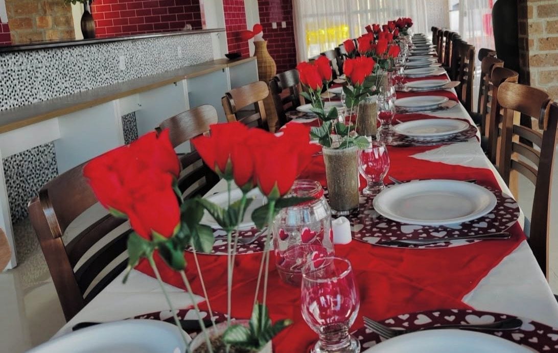 Una larga mesa de comedor adornada con rosas rojas, platos blancos y cubertería de vidrio.