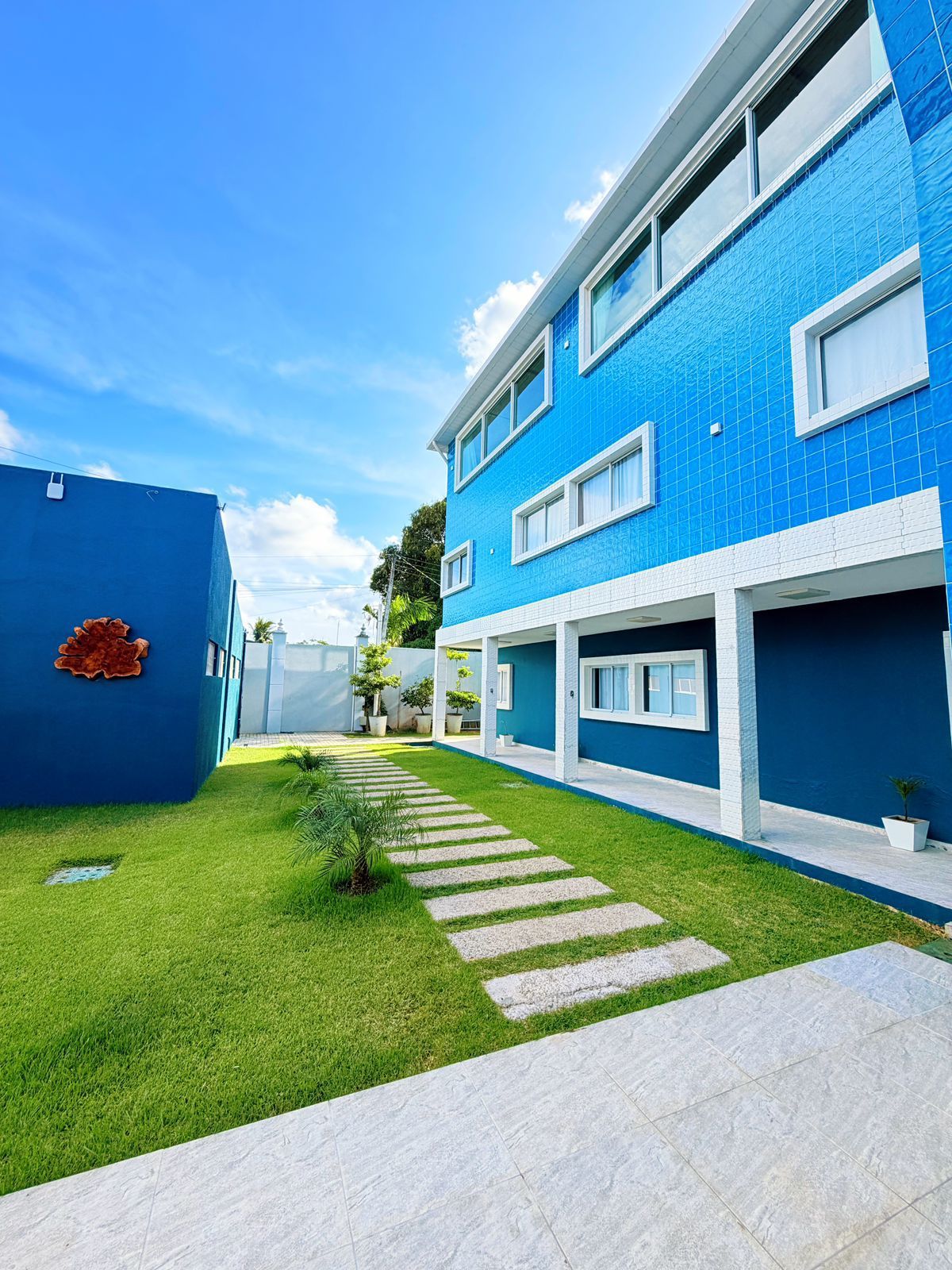 Un edificio moderno con fachada azul, entrada pavimentada y un pequeño césped.
