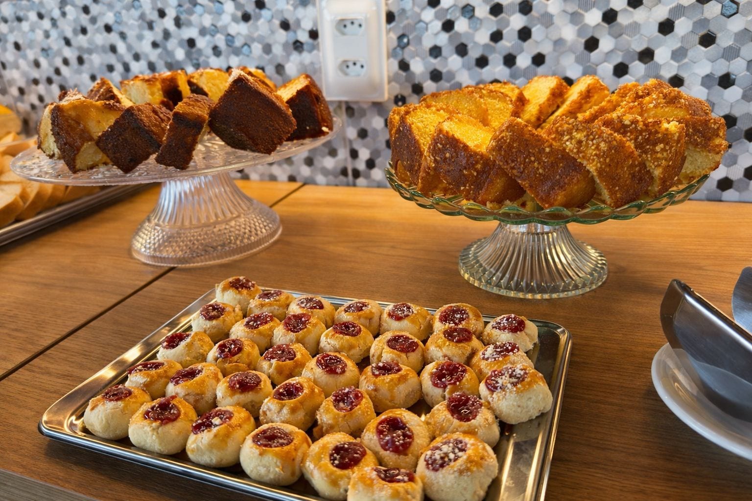 A variety of baked goods on display, including a cake on a glass stand and a tray of scones with jam.