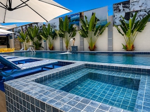 En swimmingpool med flisegange, liggestole og krukker med planter.