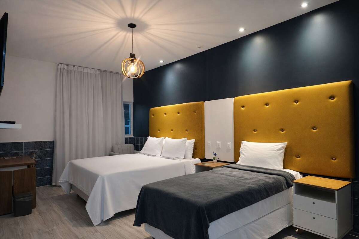 Een moderne hotelkamer met twee bedden, een nachtkastje, een bureau en een groot raam met gordijnen.