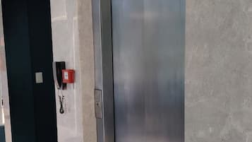Un ascensor con pantalla digital, señal de accesibilidad para sillas de ruedas y un teléfono rojo de emergencia.