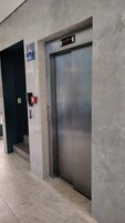 Um elevador com visor digital, sinal de acessibilidade para cadeiras de rodas e telefone de emergência vermelho.
