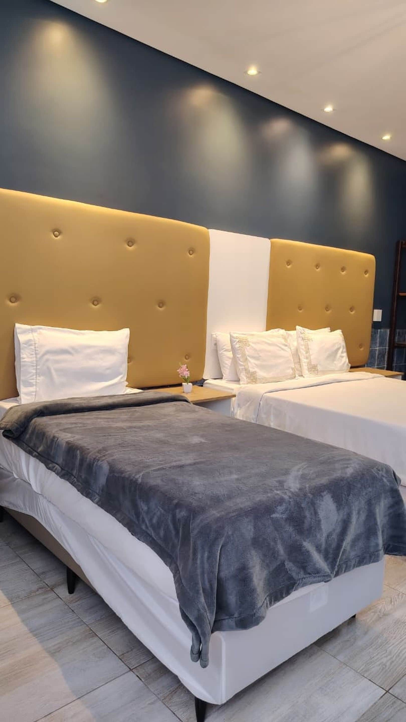 A hotel room with two beds, a large headboard, and a small table with a flower.