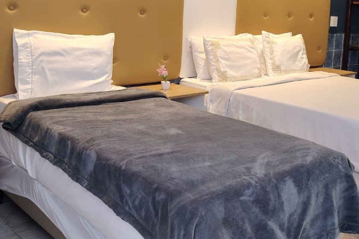 Habitación de hotel con dos camas, un cabecero grande y una pequeña mesa con una flor.