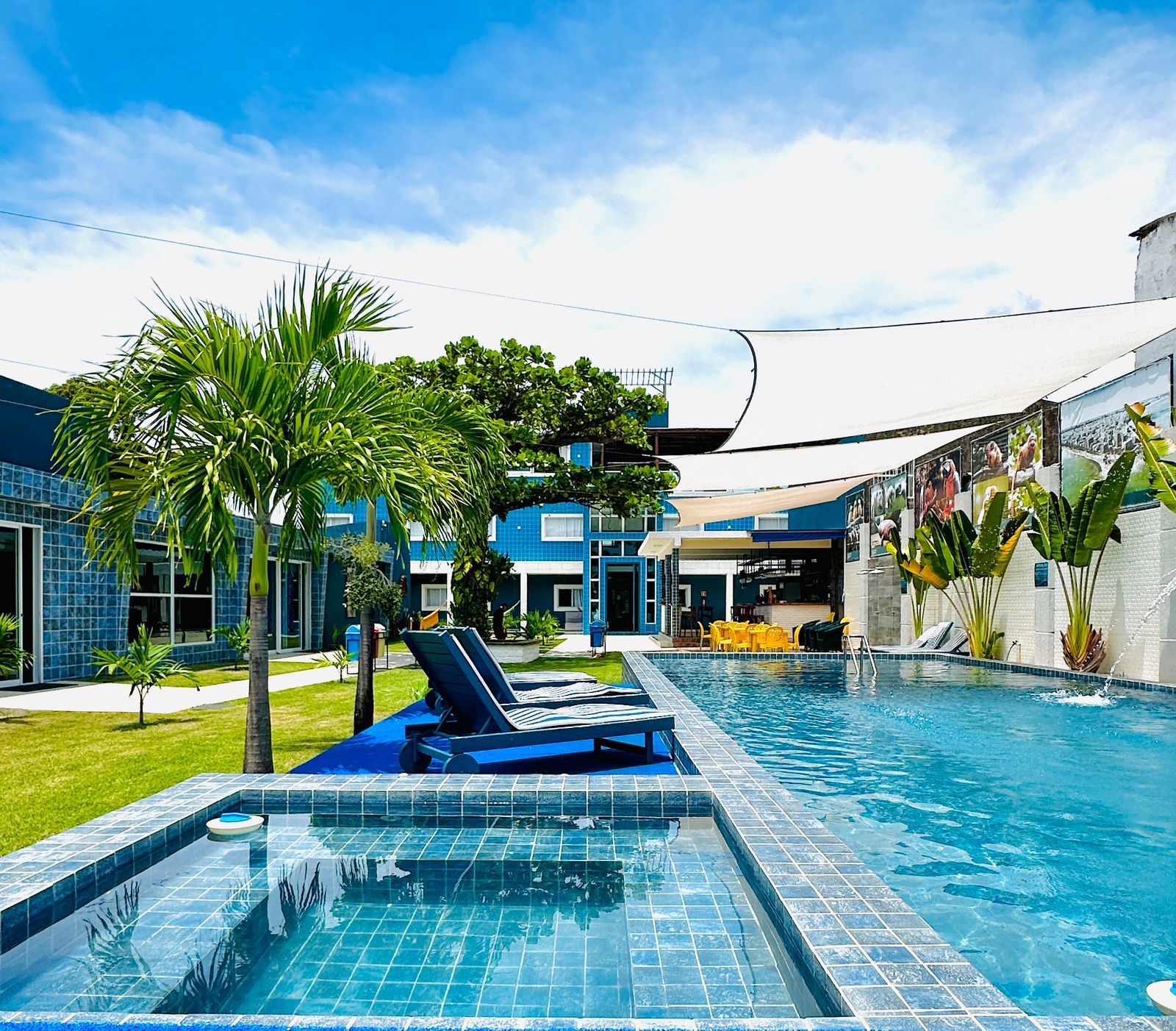 A swimming pool with lounge chairs, palm trees, and a building with blue tiles.