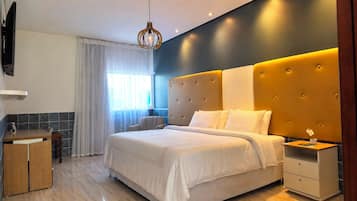 Una habitación de hotel moderna con una cama grande, una mesita de noche, un escritorio pequeño y una silla.
