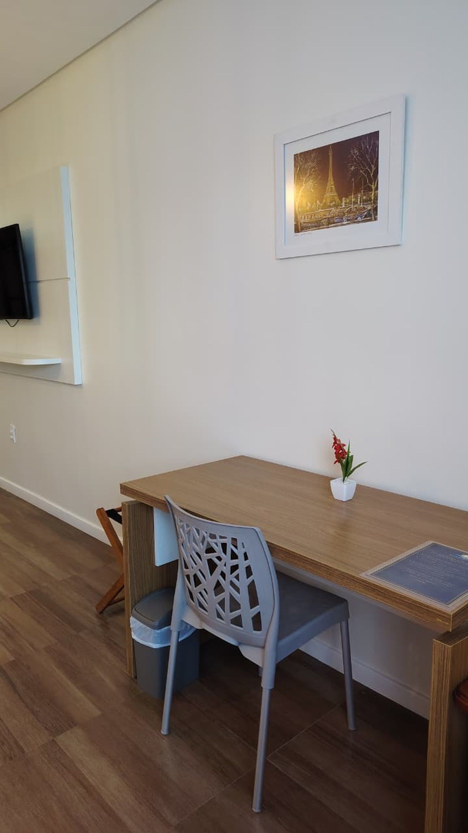 Una habitación moderna con un escritorio de madera, una silla gris, una pequeña planta en maceta y un cuadro en la pared.