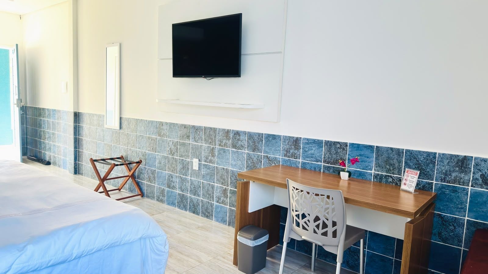 Ein Hotelzimmer mit Bett, Schreibtisch, Stuhl, Wandfernseher und einer gefliesten Spritzschutzleiste.