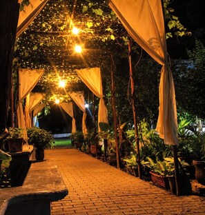 Un sentier extérieur revêtu de briques, bordé de plantes en pot et agrémenté de structures décoratives en tissu.