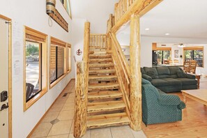 Eine Holztreppe führt zu einer oberen Etage, ein sofa mit grünem Muster und ein Essbereich mit Blick ins Freie.