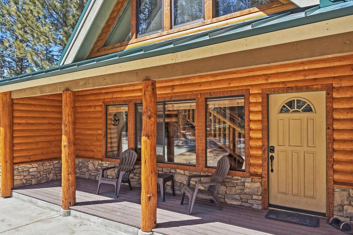 A log cabin with a porch, stone foundation, and a door with a window above it.