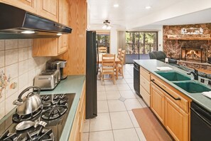 A kitchen with a gas stove, toaster, and a stone fireplace. - 1 Mile Away From Snow Summit! PET FRIENDLY! Game Room W/ Pool + Ping Pong Combo Table & Foosball! Fenced Back Yard! Deck W/ Patio Furniture & Propane BBQ! (Big Bear Lake)